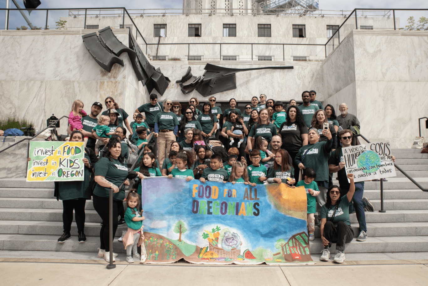 Group of advocates, kids and adults, holding signs in support of Food for All Oregonians on the Capitol steps in Salem.